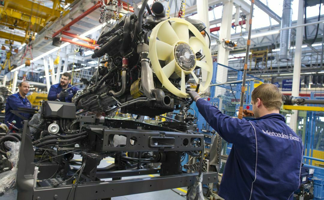 Ein Daimler-Mitarbeiter montiert einen Motorblock in das Fahrwerk eines Lastkraftwagens