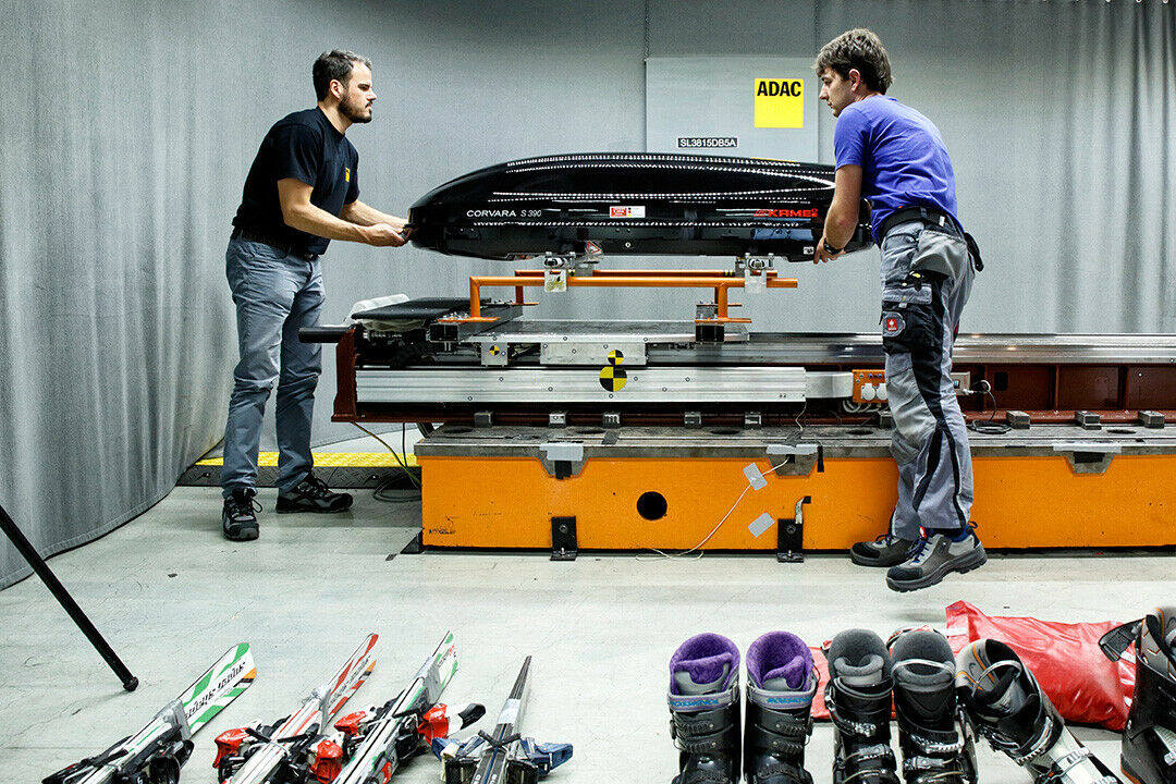Techniker des ADAC befestigen eine Dachbox auf dem Crash-Schlitten