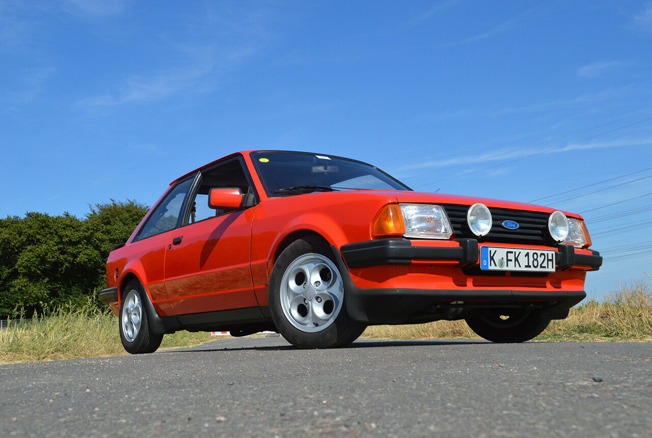 Das Sportmodell Ford Escort XR3 ist an der aerodynamische Verkleidungen der Radläufe sowie seine Frontspoilerlippe im Rückspiegel erkennbar