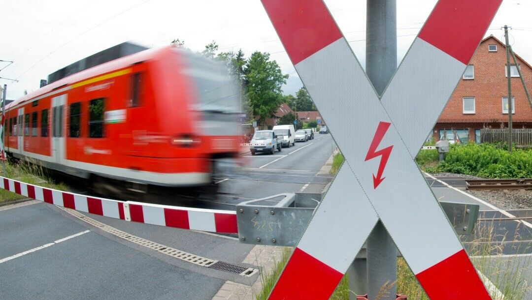 Eine Regionalbahn fährt an einem Bahnübergang mit geschlossenen Schranken vorbei